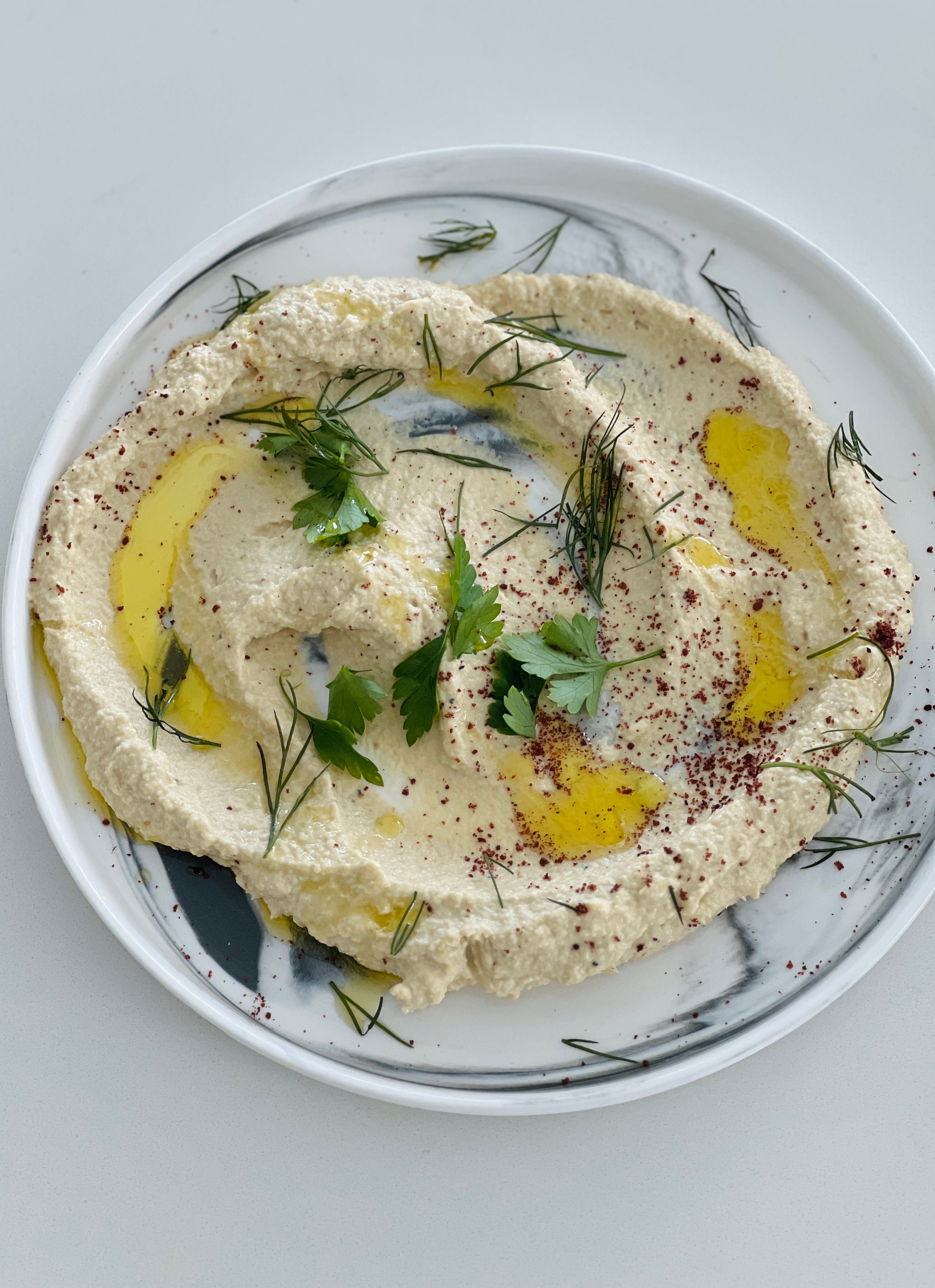 Plate of creamy artichoke hummus made with 'Everything Tahini', garnished with a drizzle of olive oil and fresh green herbs, ready to be paired with crunchy veggie crudités